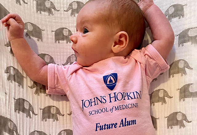 A baby wearing a pink onesie that reads, &quot;Johns Hopkins School of Medicine Future Alumna.&quot;
